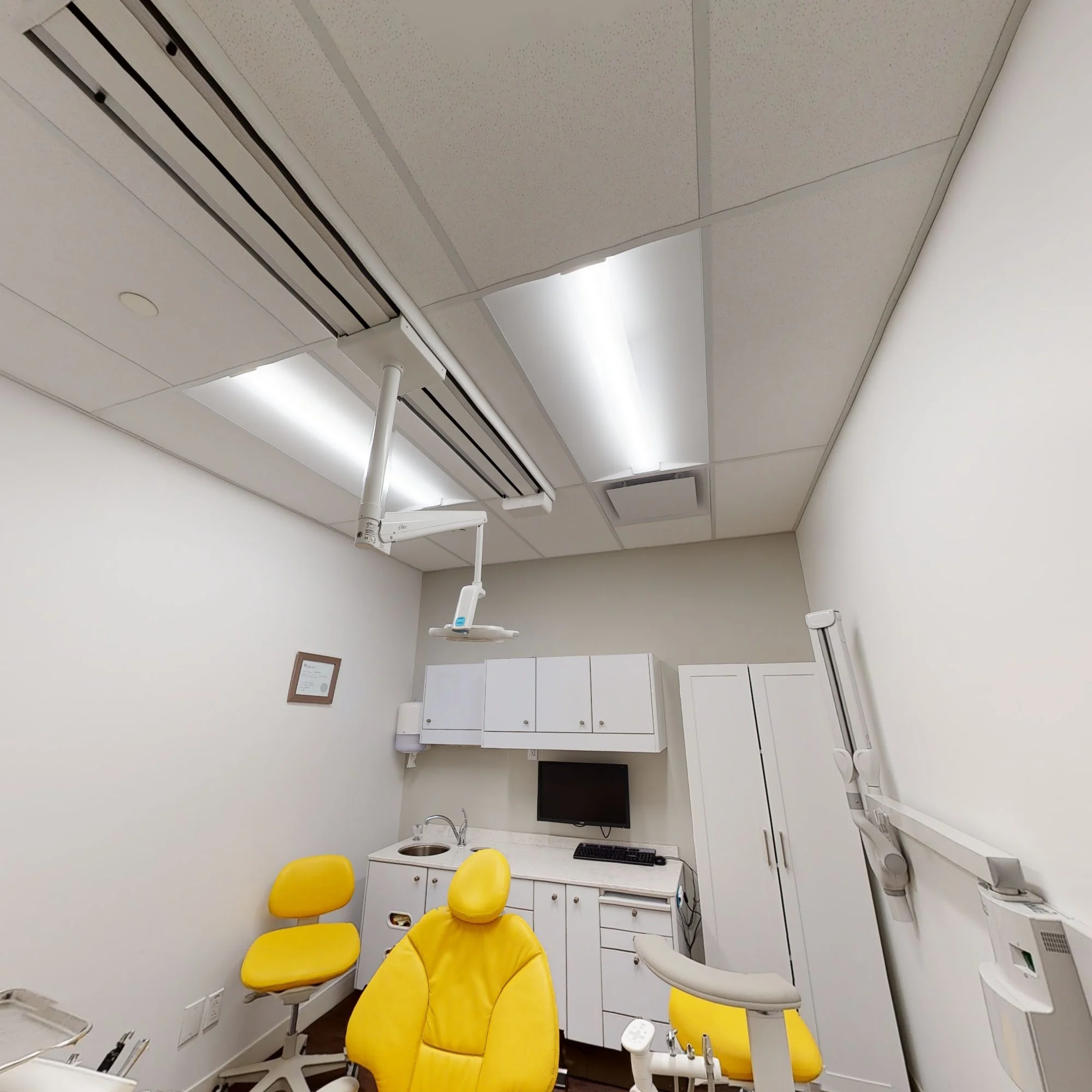 Salle de soins de la clinique avec fauteuil jaune et éclairage dentaire.
