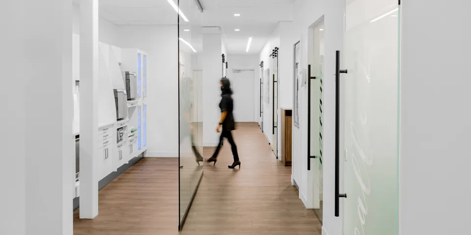Couloir lumineux avec plancher effet bois et cloisons vitrées.