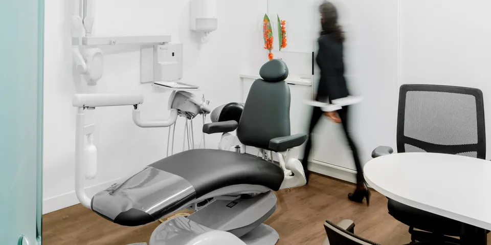 Fauteuil dentaire gris et équipements de soins à côté d’un bureau de consultation.