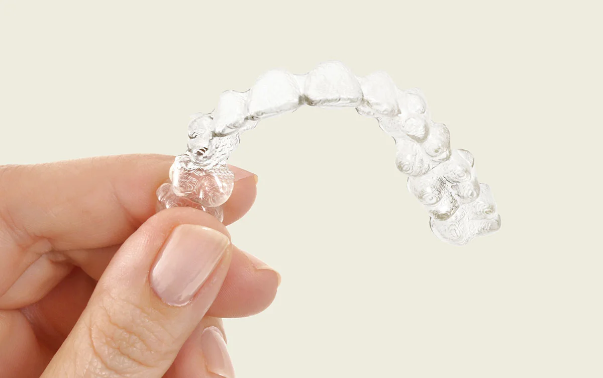 Une gouttière transparente Invisalign tenue entre les doigts